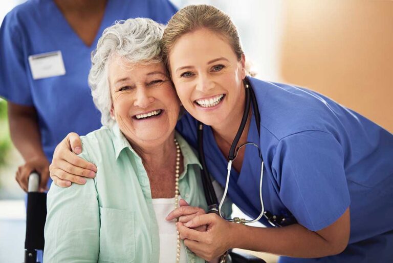 Family member and older adult talk beside a furnished assisted living room window.