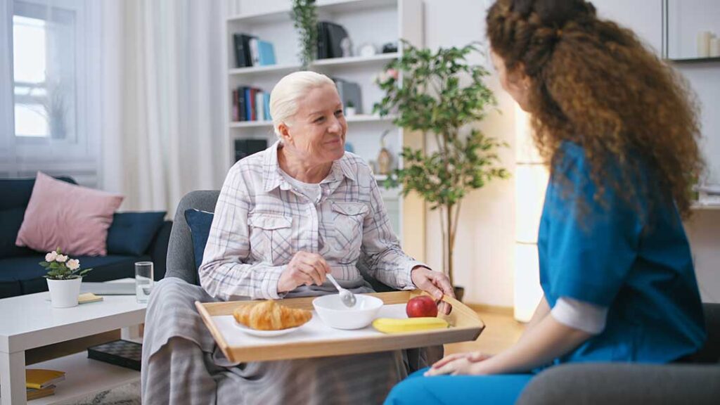 Older adult and family member organize labeled clothing, toiletries, photographs, and a small lamp in a bedroom.