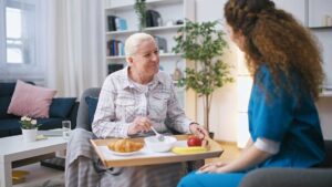 Older adult and family member organize labeled clothing, toiletries, photographs, and a small lamp in a bedroom.
